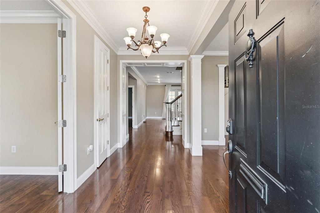 A foyer with hardwood floors leads to a hallway featuring a chandelier and staircase — 5210 HAMMOCK CIRCLE, ST CLOUD, FL