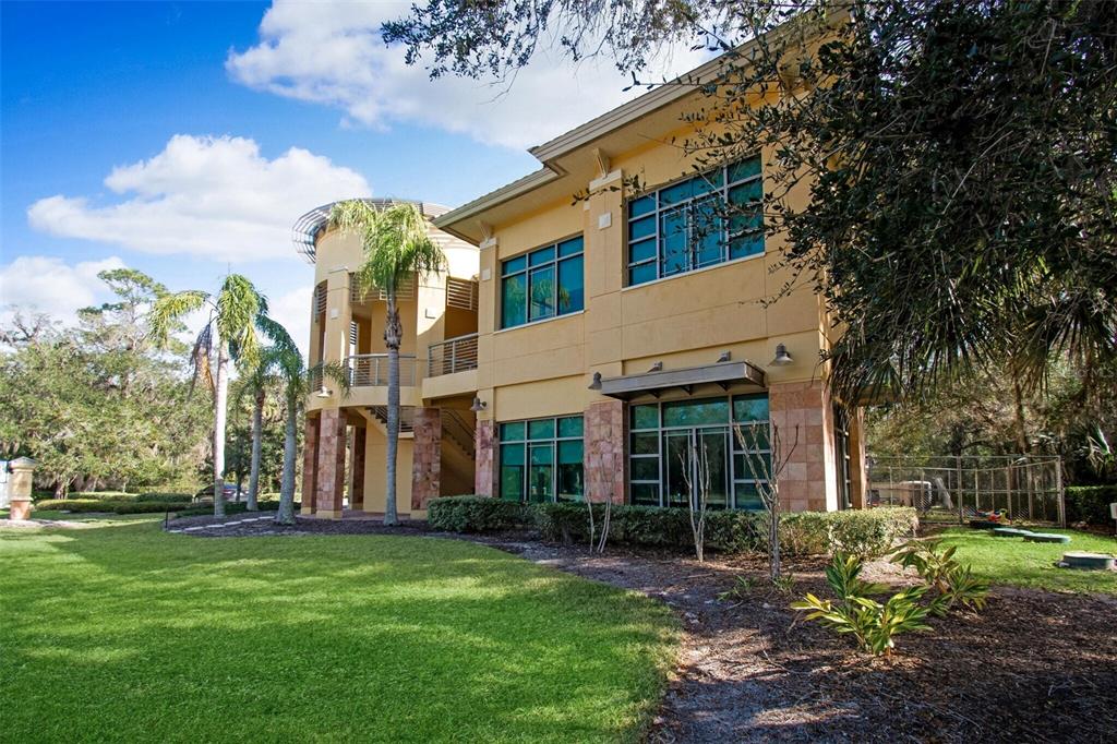 A two-story tan building with large windows and a curved balcony sits on a lawn — 6 MERIDIAN HOME LANE UNIT 101, PALM COAST, FL