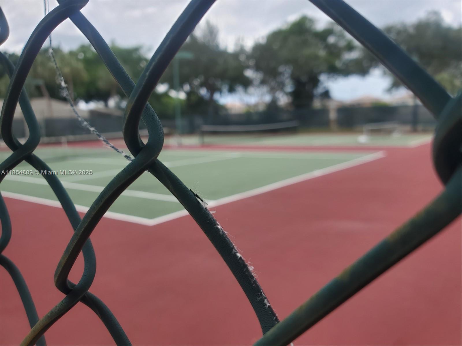A view of a tennis court is seen through a chain-link fence — 3940 Inverrary Blvd # A, Lauderhill FL 33319, LAUDERHILL, FL