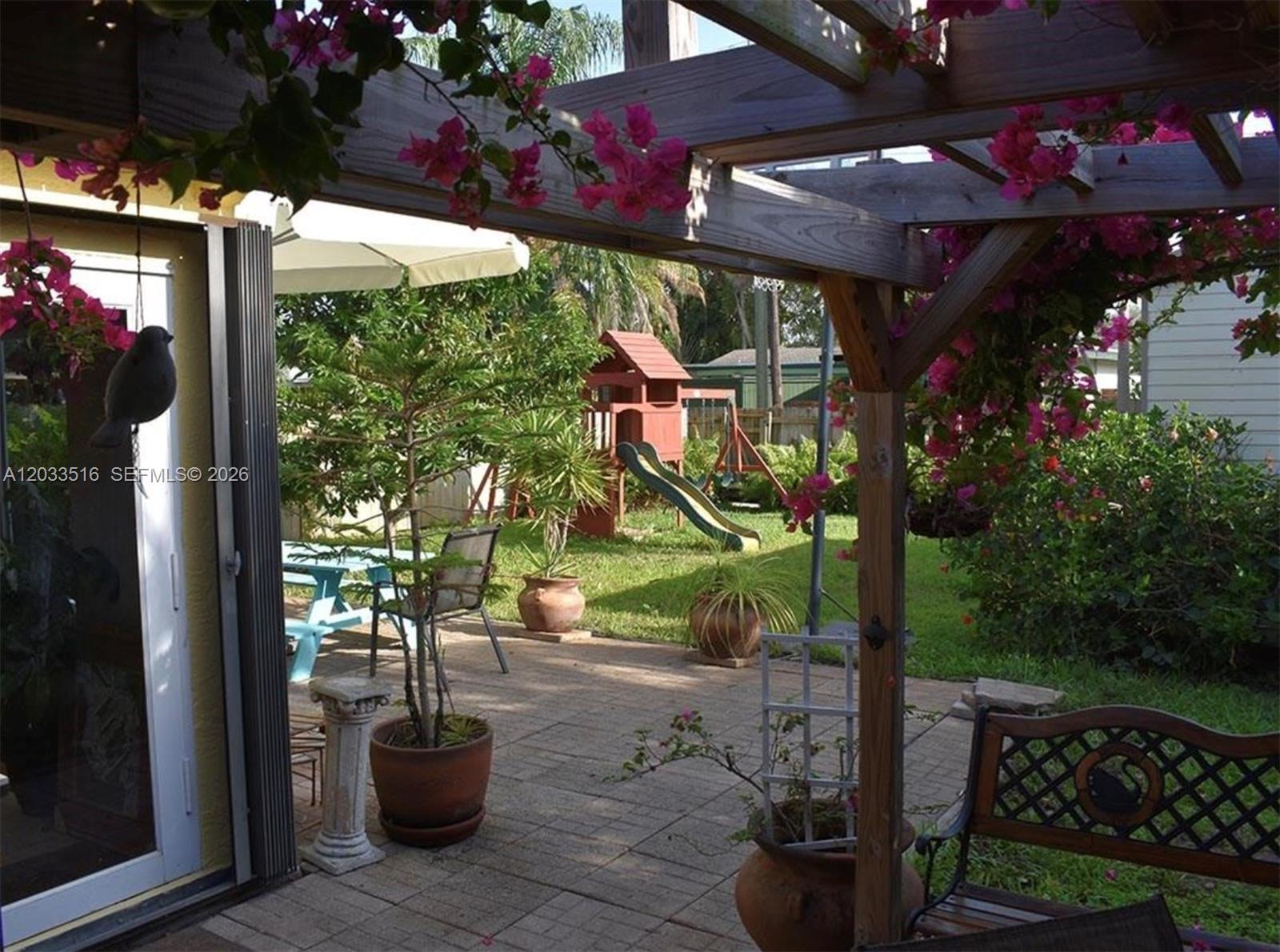 A patio with a wooden pergola, potted plants, and a children's playset in the yard — 4415 Tyler St # 4415, Hollywood FL 33021, HOLLYWOOD, FL