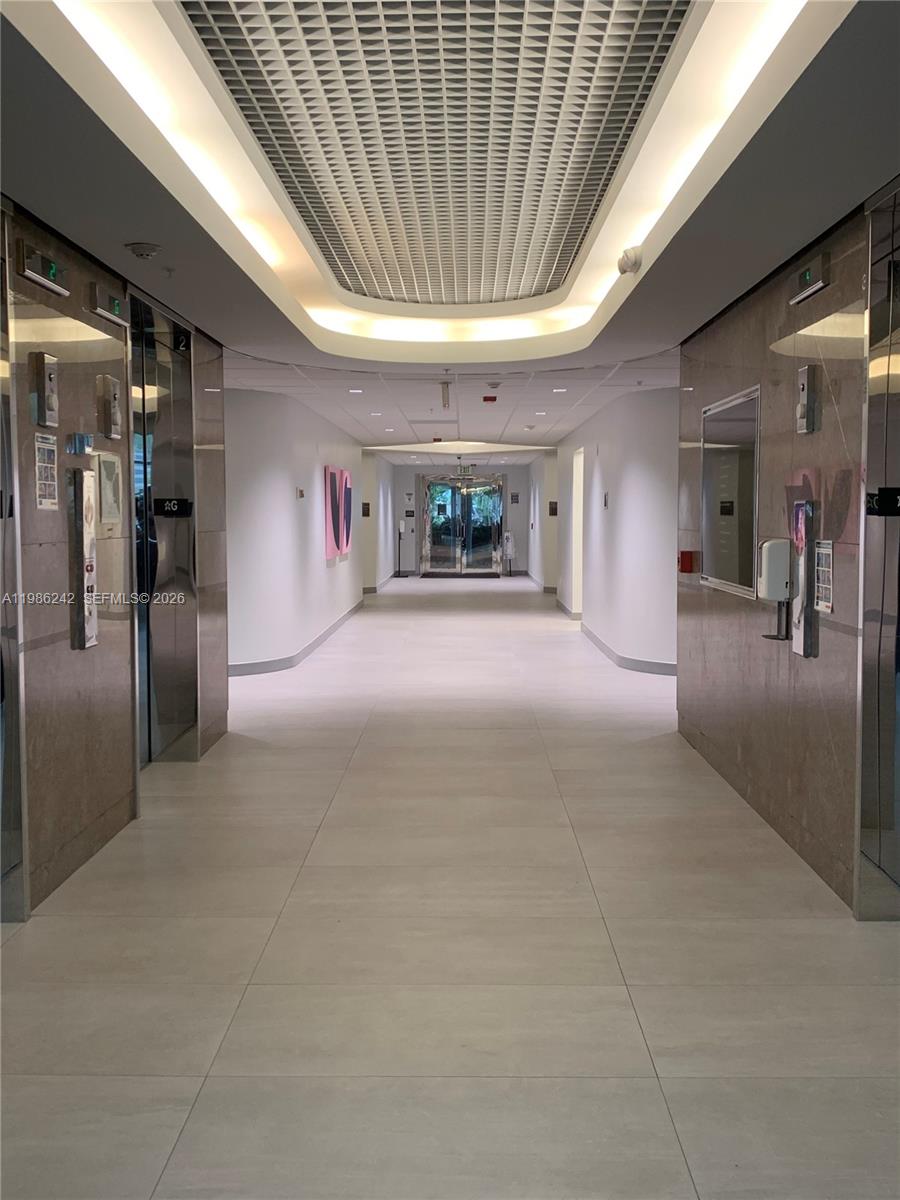 A modern hallway features marble walls, elevator doors, and a recessed ceiling with cove lighting — 5959 Waterford District Dr # 200, Miami FL 33126, MIAMI, FL