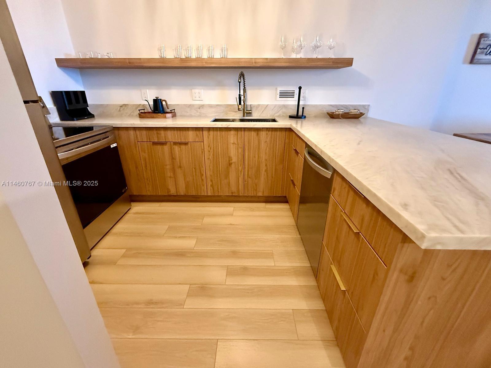 A kitchen features light wood cabinets, marble countertops, a stainless steel sink, and floating shelves — 2301 Collins Ave # 1121, Miami Beach FL 33139, MIAMI BEACH, FL