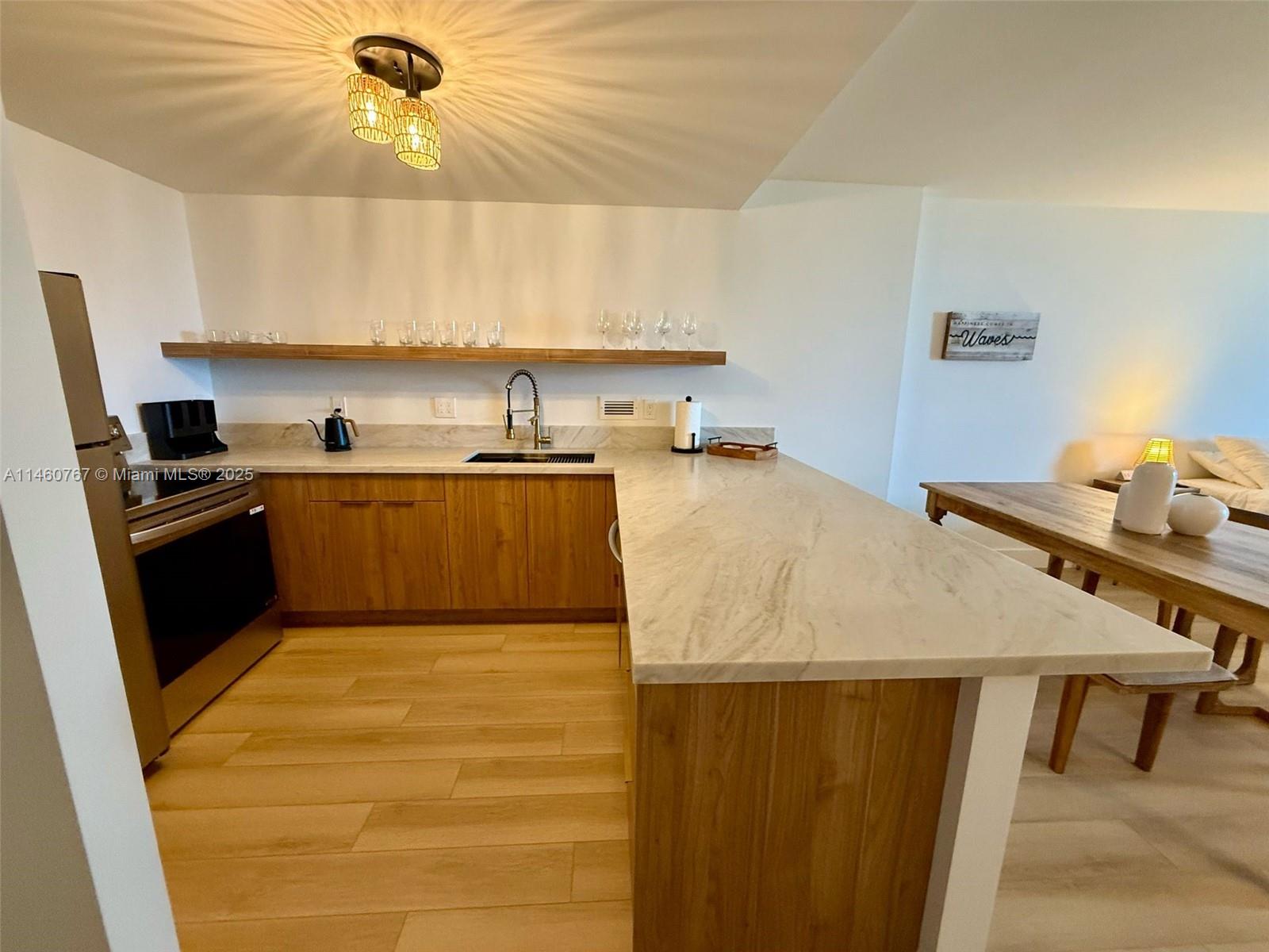 A modern kitchen features light wood cabinets, a marble countertop, and an open shelf — 2301 Collins Ave # 1121, Miami Beach FL 33139, MIAMI BEACH, FL