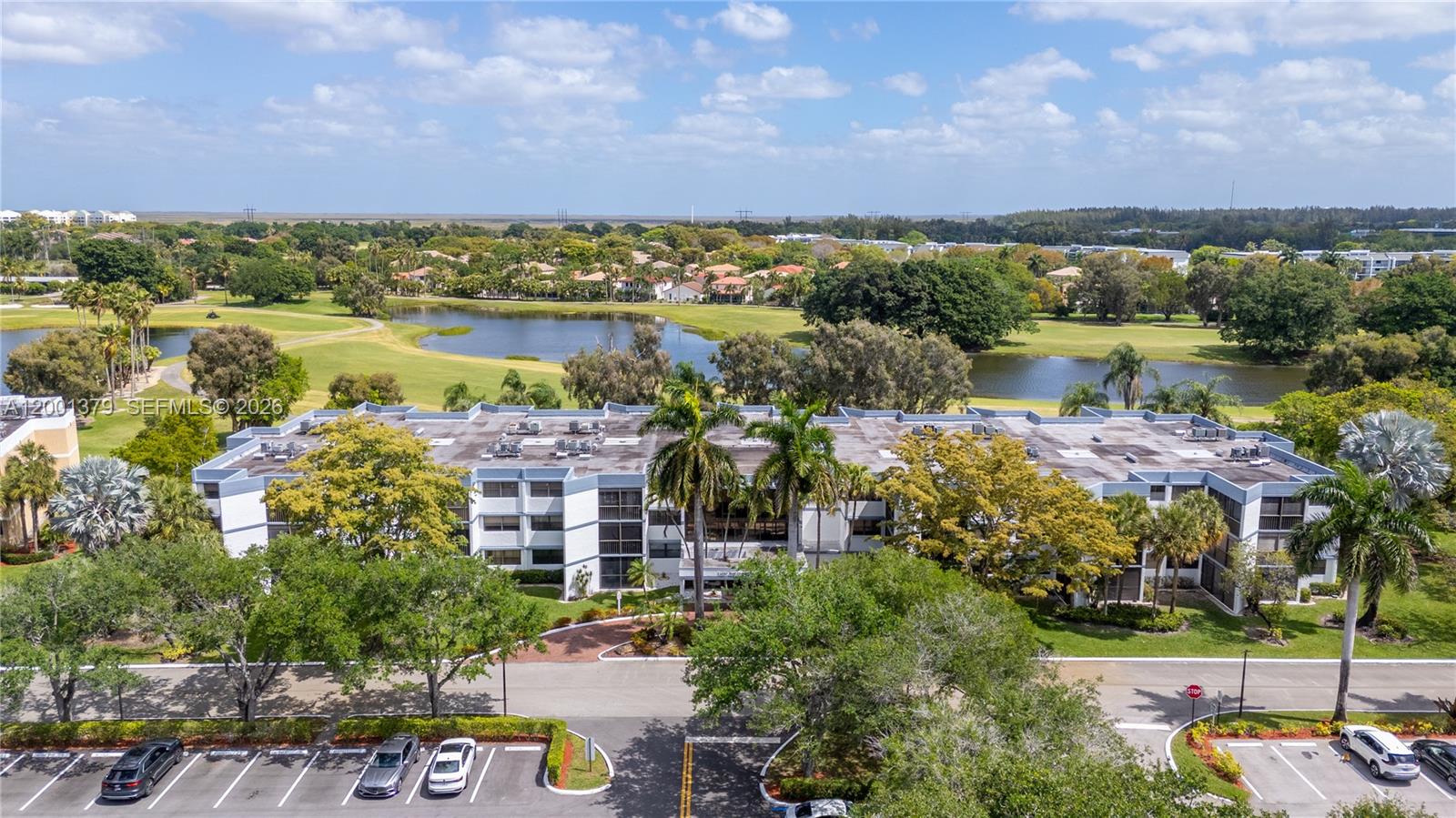 An aerial view shows a multi-story apartment building surrounded by trees, a lake, and a golf course — 16251 Golf Club Rd # 311, Weston FL 33326, WESTON, FL