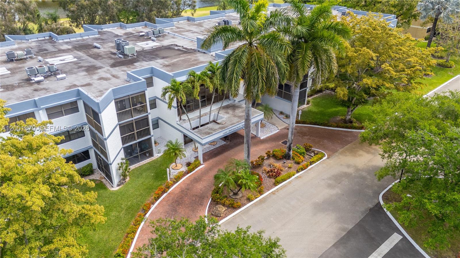 An aerial view shows a multi-story apartment building with a brick driveway and palm trees — 16251 Golf Club Rd # 311, Weston FL 33326, WESTON, FL