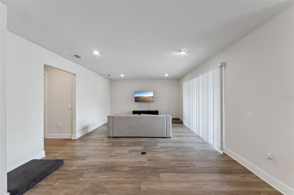 A living room with light wood-look flooring, white walls, a gray sofa, and vertical blinds — 4008 MEANDERING BAY DRIVE, APOPKA, FL