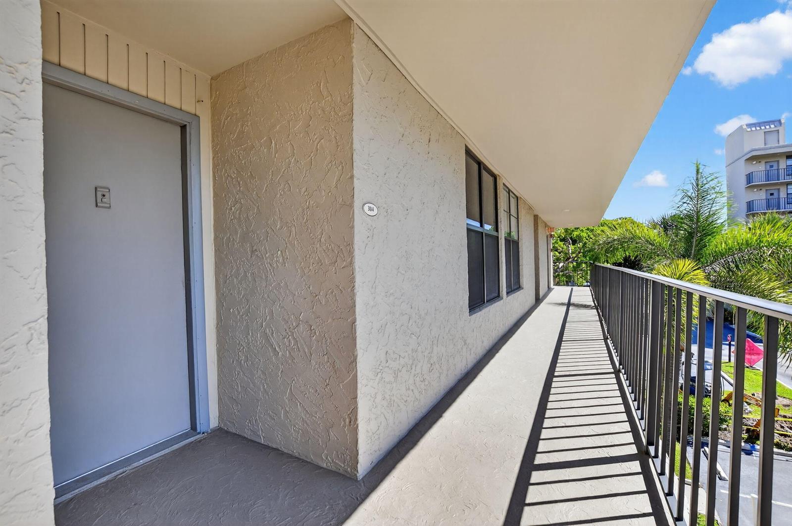 An exterior walkway with a grey door labeled 304, stucco walls, and a metal railing — 11 Royal Palm Way # 3040, Boca Raton FL 33432, BOCA RATON, FL