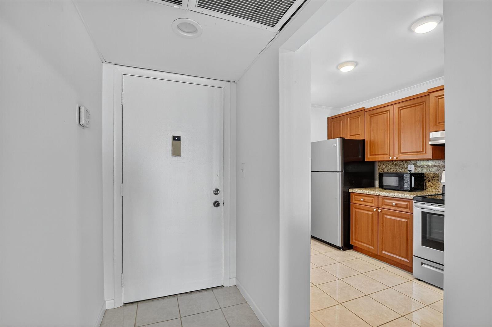 A white front door opens into a tiled entryway adjacent to a kitchen with wood cabinets — 11 Royal Palm Way # 3040, Boca Raton FL 33432, BOCA RATON, FL