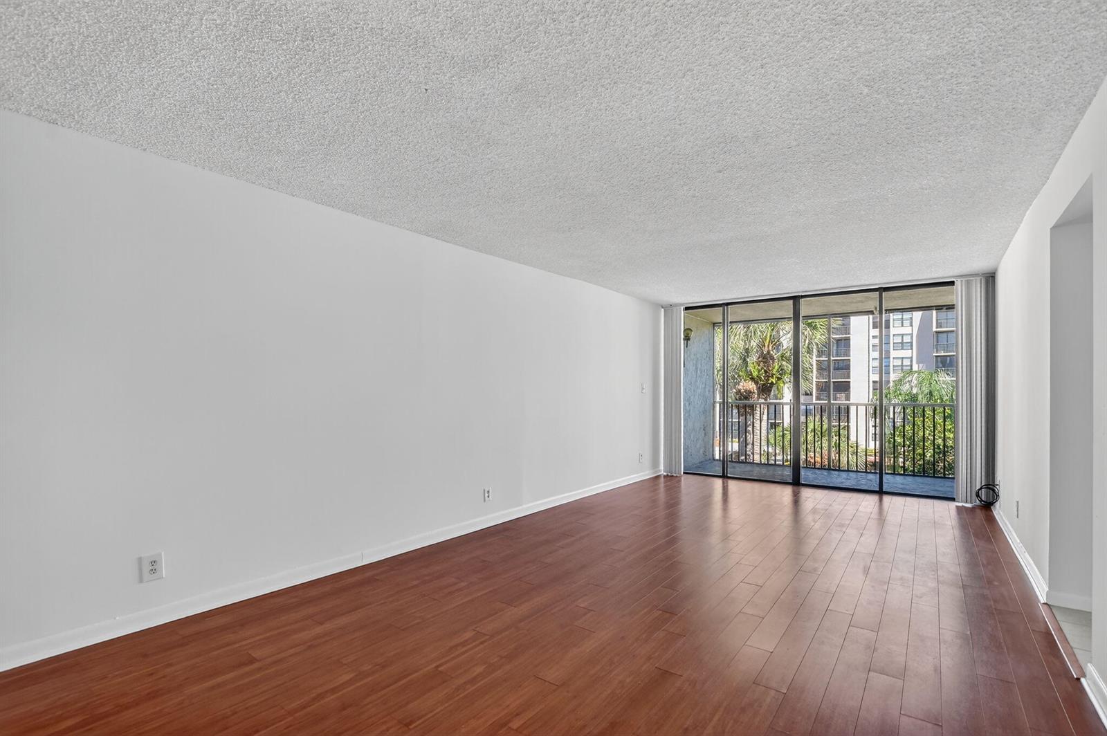 An empty living room features dark wood flooring, white walls, and a sliding glass balcony door — 11 Royal Palm Way # 3040, Boca Raton FL 33432, BOCA RATON, FL