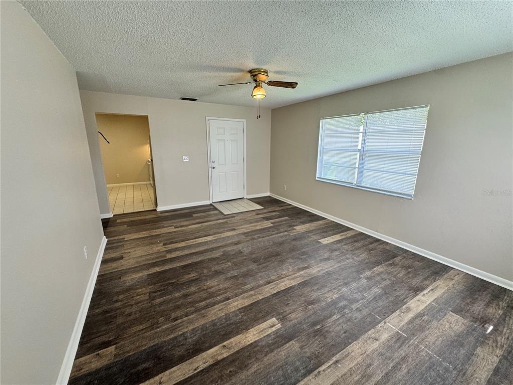 An empty living room features wood-look flooring, a ceiling fan, and a white entry door — 1001 CRAWFORD STREET, LEESBURG, FL