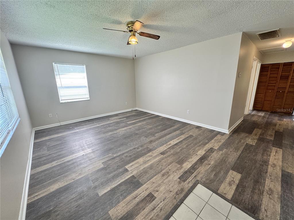 An empty room features gray wood-look flooring, light-colored walls, a ceiling fan, and a window — 1001 CRAWFORD STREET, LEESBURG, FL
