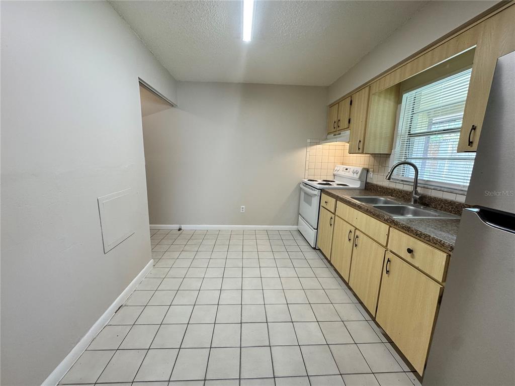A kitchen features light wood cabinets, tiled flooring, a white stove, and a double sink — 1001 CRAWFORD STREET, LEESBURG, FL
