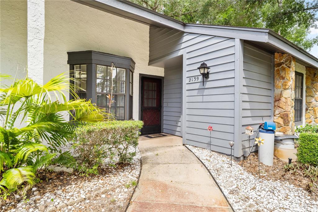 A concrete walkway leads to the front entrance of a house with gray siding — 2139 SEA PINES COURT, SPRING HILL, FL