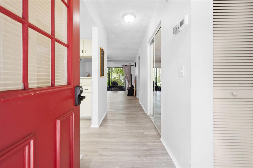 An open red front door reveals a hallway with light wood-look flooring and white walls — 2139 SEA PINES COURT, SPRING HILL, FL