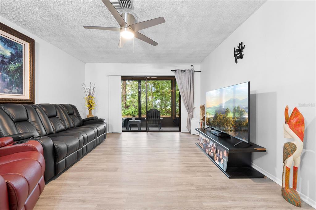 A living room features light wood-look flooring, a black leather sofa, and a television console — 2139 SEA PINES COURT, SPRING HILL, FL