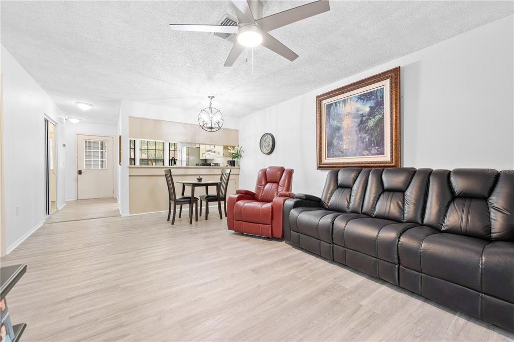 A living room with light wood-look flooring, a black leather sofa, and a red recliner — 2139 SEA PINES COURT, SPRING HILL, FL