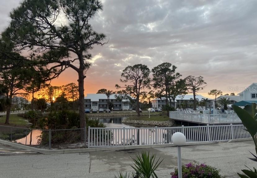 A sunset view over a pond with apartment buildings, trees, and a white fence — 6800 PLACIDA ROAD UNIT 290, ENGLEWOOD, FL