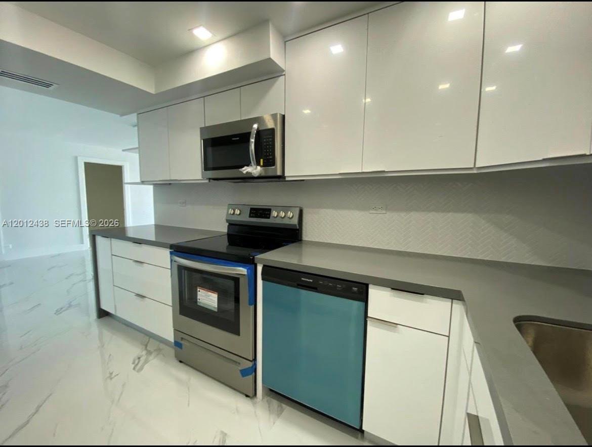 A modern kitchen features white cabinets, stainless steel appliances, and gray countertops — 6039 Collins Ave # 1033, Miami Beach FL 33140, MIAMI BEACH, FL
