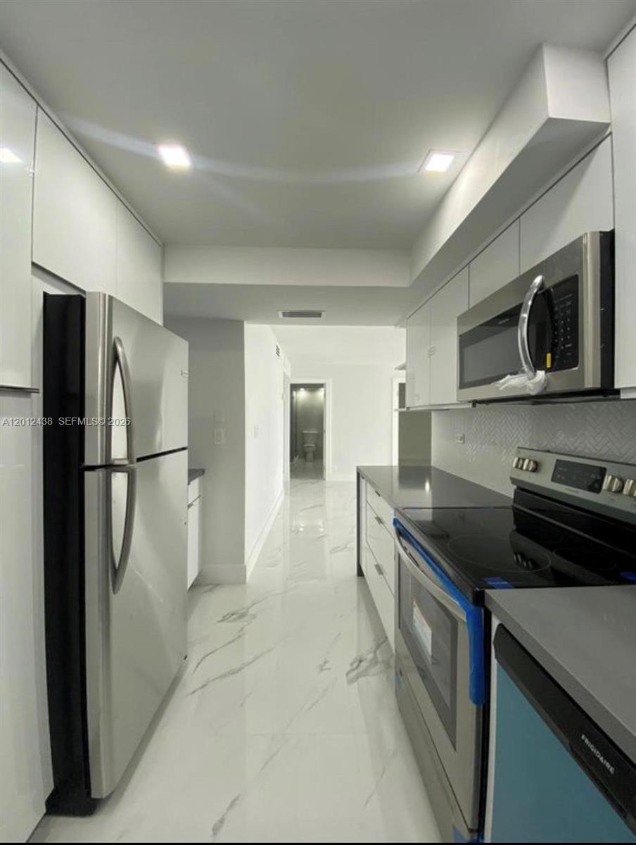 A narrow galley kitchen features white cabinets, stainless steel appliances, and light marble-patterned flooring — 6039 Collins Ave # 1033, Miami Beach FL 33140, MIAMI BEACH, FL