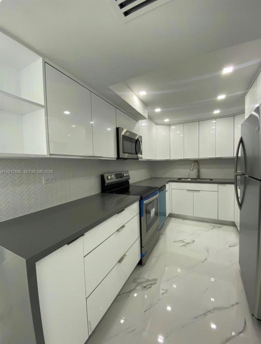 A modern kitchen features white cabinets, dark gray countertops, stainless steel appliances, and marble flooring — 6039 Collins Ave # 1033, Miami Beach FL 33140, MIAMI BEACH, FL