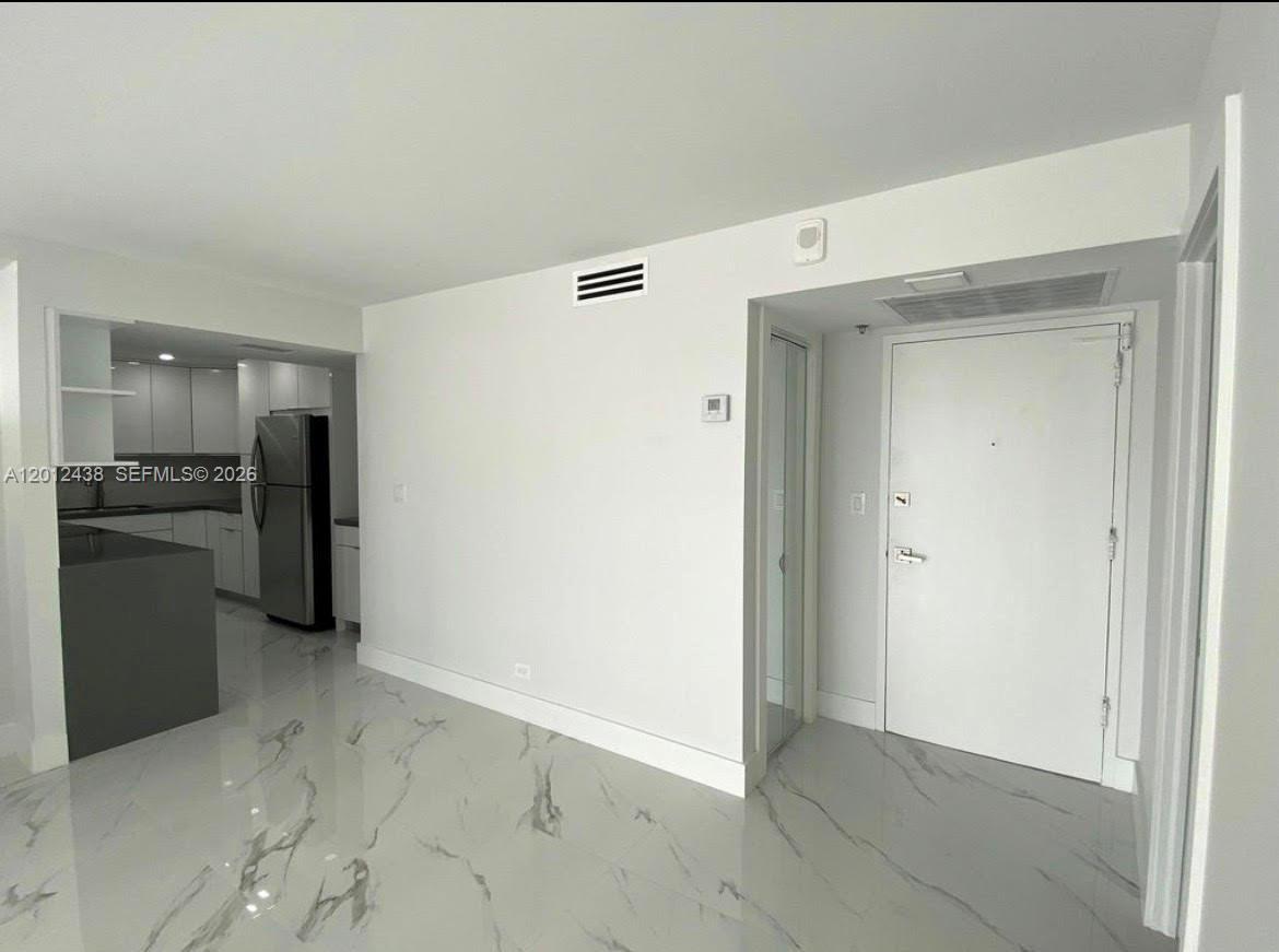 A white-walled room features light-colored marble flooring and a view into a modern kitchen — 6039 Collins Ave # 1033, Miami Beach FL 33140, MIAMI BEACH, FL