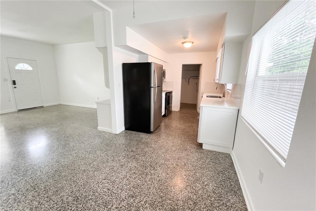 A kitchen with white cabinets, a black refrigerator, and speckled flooring opens to a room — 70 GRIGGS AVENUE, CASSELBERRY, FL