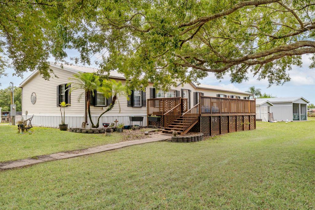 A single-story manufactured home features a large wooden deck and a stone walkway — 11301 SW Fox Brown Road, FL 34956, FL