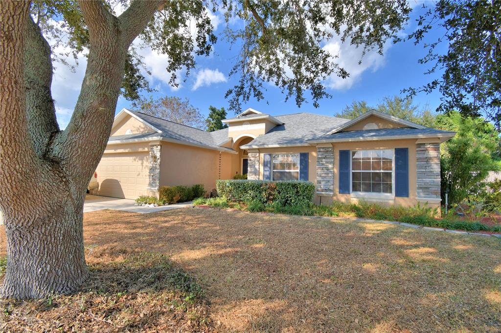 A tan single-story house with a two-car garage, stone accents, and a concrete driveway — 3425 STONEWAY DRIVE, LAKELAND, FL