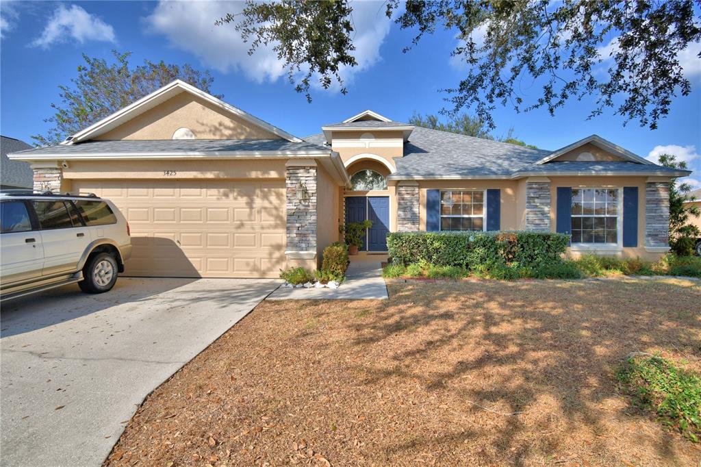 A single-story suburban house with a tan stucco exterior, stone accents, and a two-car garage — 3425 STONEWAY DRIVE, LAKELAND, FL