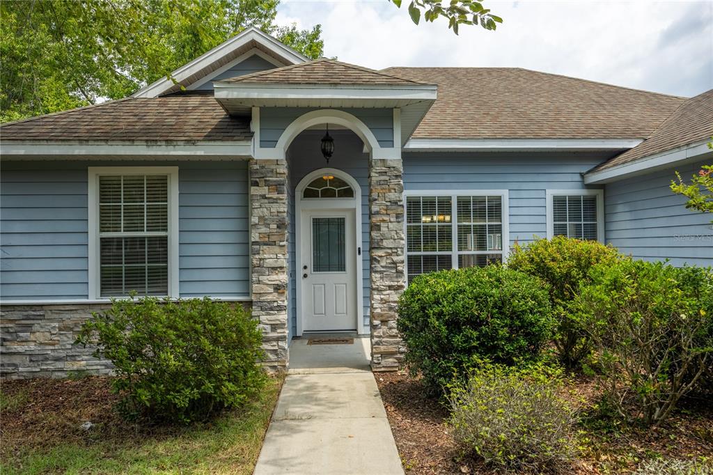 A blue-sided house features a stone-accented entryway with a white front door and walkway — 9004 SW 79TH AVENUE, GAINESVILLE, FL