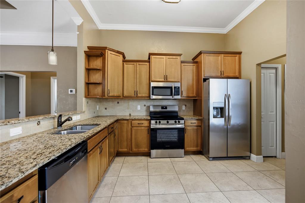 A kitchen features wood cabinets, granite countertops, stainless steel appliances, and tile flooring — 9004 SW 79TH AVENUE, GAINESVILLE, FL