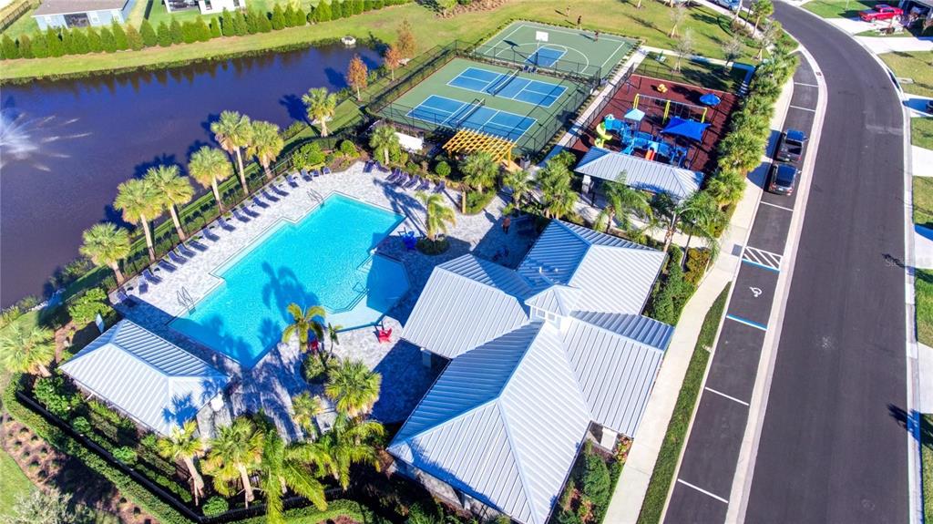 An aerial view of a community pool, tennis courts, playground, and clubhouse next to water — 7005 166TH PLACE E, PARRISH, FL