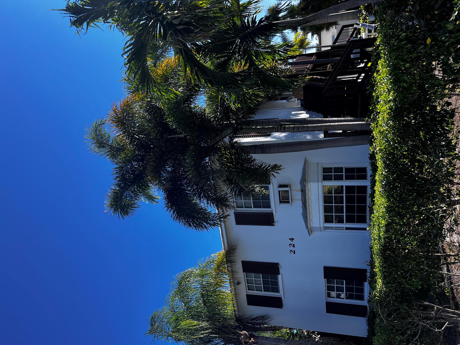 A two-story white building with dark shutters and palm trees under a clear blue sky — 224 Conniston Road # 2, West Palm Beach FL 33405, WEST PALM BEACH, FL