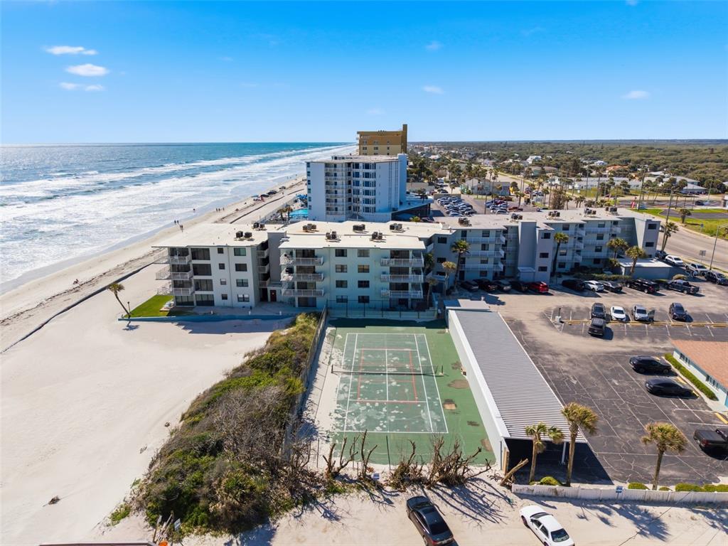 An aerial view shows a beachfront condominium complex with a tennis court and parking lot — 1571 S ATLANTIC AVENUE UNIT 2120, NEW SMYRNA BEACH, FL