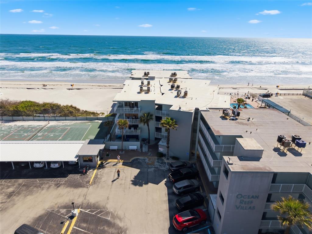 An aerial view shows the Ocean Reef Villas beachfront property with a parking lot and tennis court — 1571 S ATLANTIC AVENUE UNIT 2120, NEW SMYRNA BEACH, FL