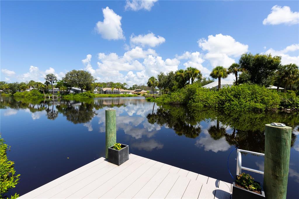 A wooden dock with two pilings and planters overlooks a calm canal and lush vegetation — 1082 MARCH DRIVE, PORT CHARLOTTE, FL