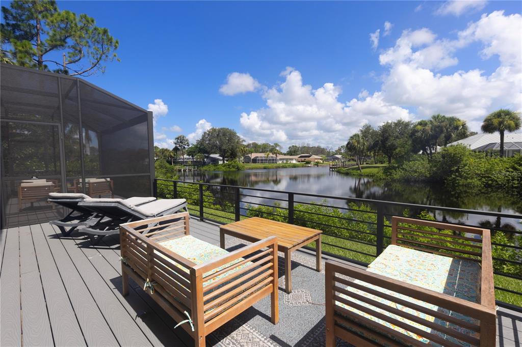 A wooden deck with patio furniture overlooks a lake surrounded by trees and houses — 1082 MARCH DRIVE, PORT CHARLOTTE, FL