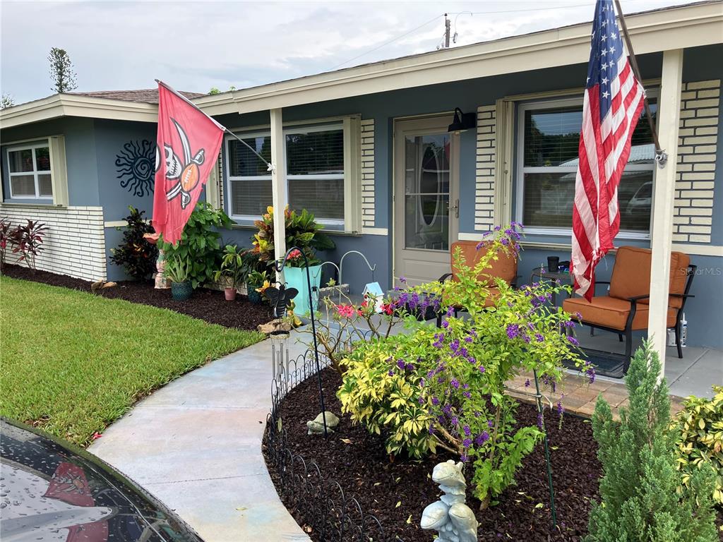 The exterior of a blue house features a front porch, landscaping, and two hanging flags — 968 62ND PLACE S, ST PETERSBURG, FL