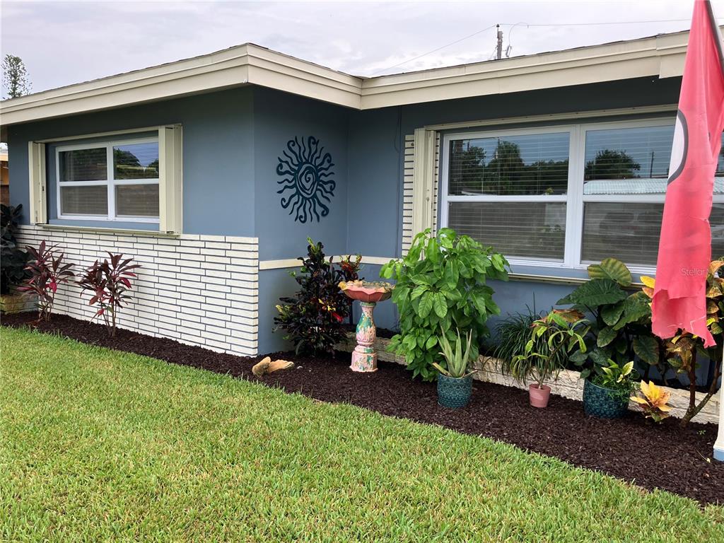 A blue house exterior features white brick siding, a sun wall decoration, and landscaped garden beds — 968 62ND PLACE S, ST PETERSBURG, FL