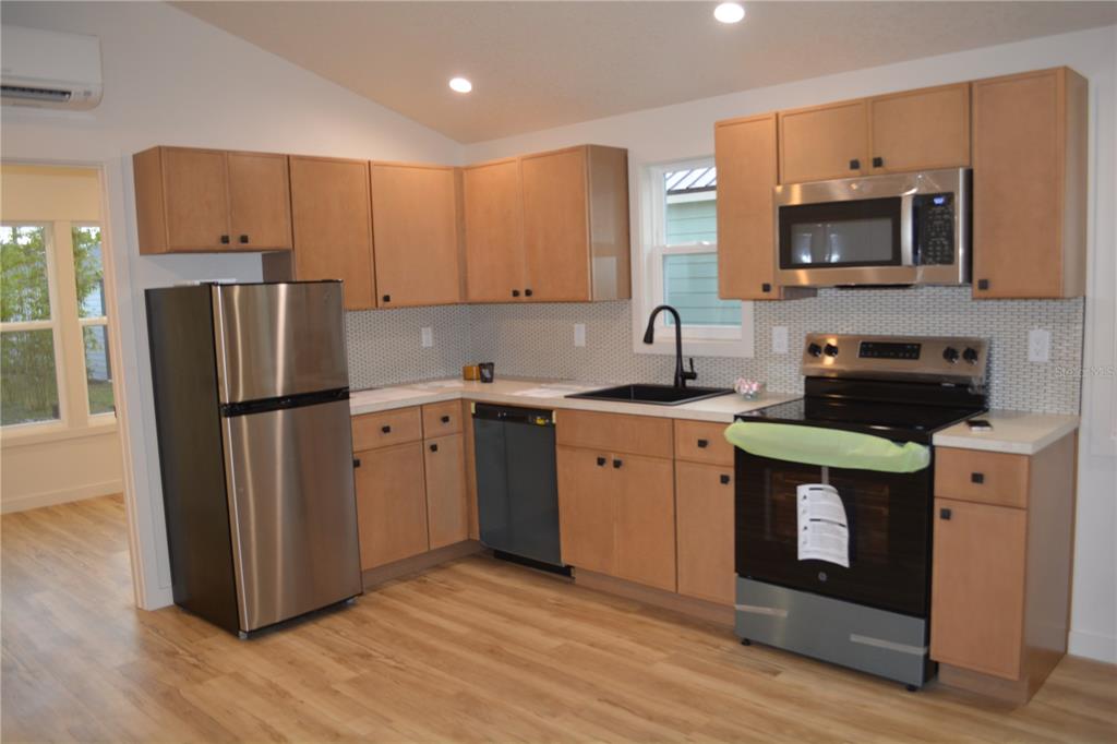 A kitchen features light wood cabinets, stainless steel appliances, a black sink, and tiled backsplash — 630 THIRD STREET STREET, OVIEDO, FL