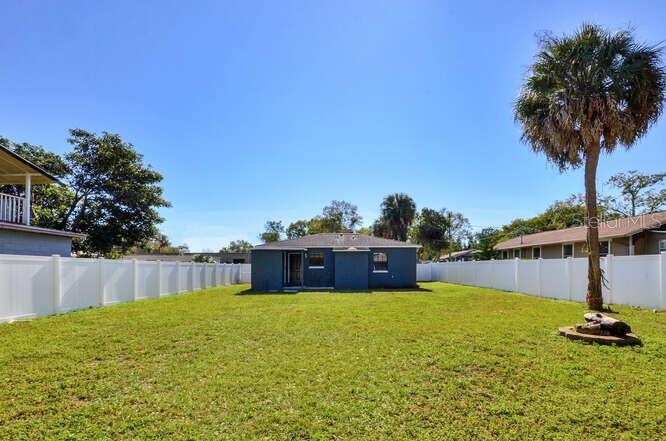 A blue house sits in the center of a large, fenced-in grassy backyard — 816 E FRIERSON AVENUE, TAMPA, FL