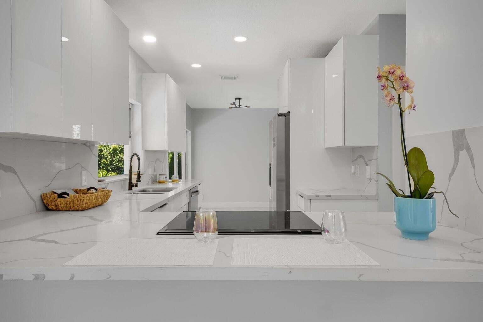 A modern kitchen features white glossy cabinets, marble-patterned countertops, and a central induction cooktop — 3740 Wilderness Way, Coral Springs FL 33065, CORAL SPRINGS, FL