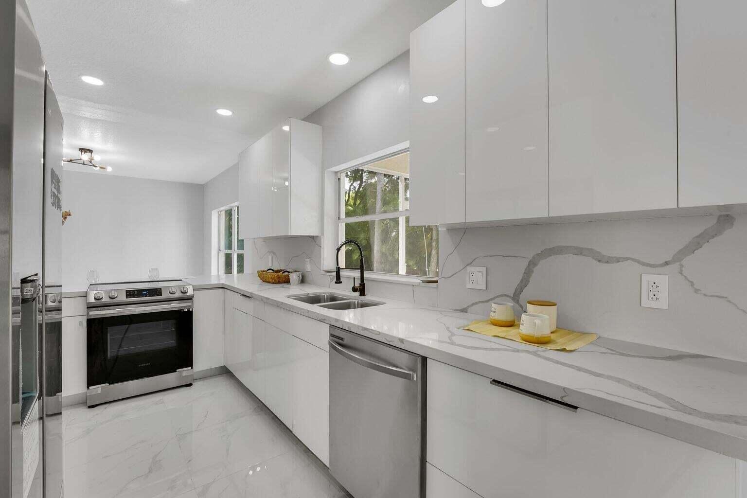 A modern kitchen features white high-gloss cabinets, marble-patterned countertops, and stainless steel appliances — 3740 Wilderness Way, Coral Springs FL 33065, CORAL SPRINGS, FL