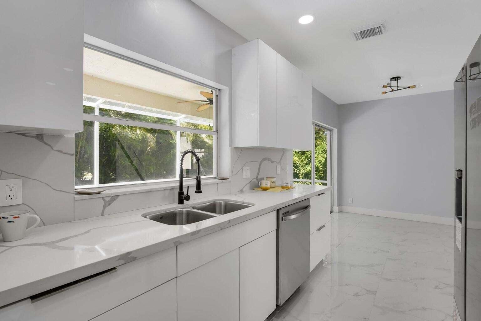 A modern kitchen features white cabinets, marble-patterned countertops, a stainless steel dishwasher, and large windows — 3740 Wilderness Way, Coral Springs FL 33065, CORAL SPRINGS, FL