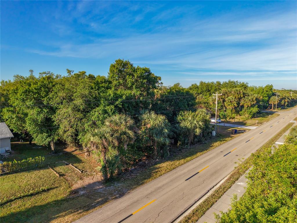An aerial view shows a vacant, tree-covered lot situated next to a paved road — 103 W 6TH STREET, LEHIGH ACRES, FL