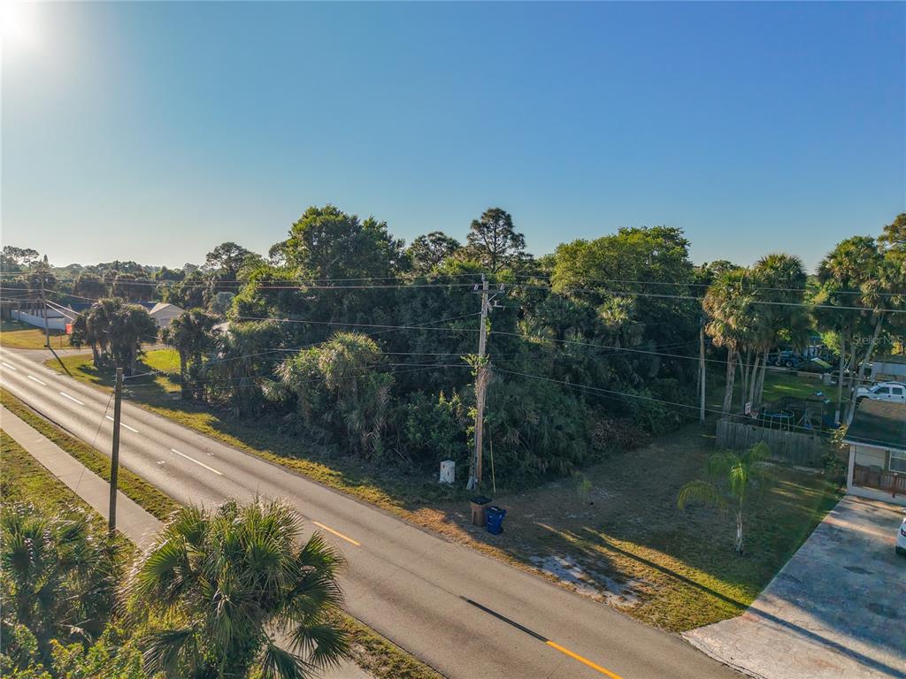 An aerial view shows a vacant, wooded lot situated next to a paved road — 103 W 6TH STREET, LEHIGH ACRES, FL