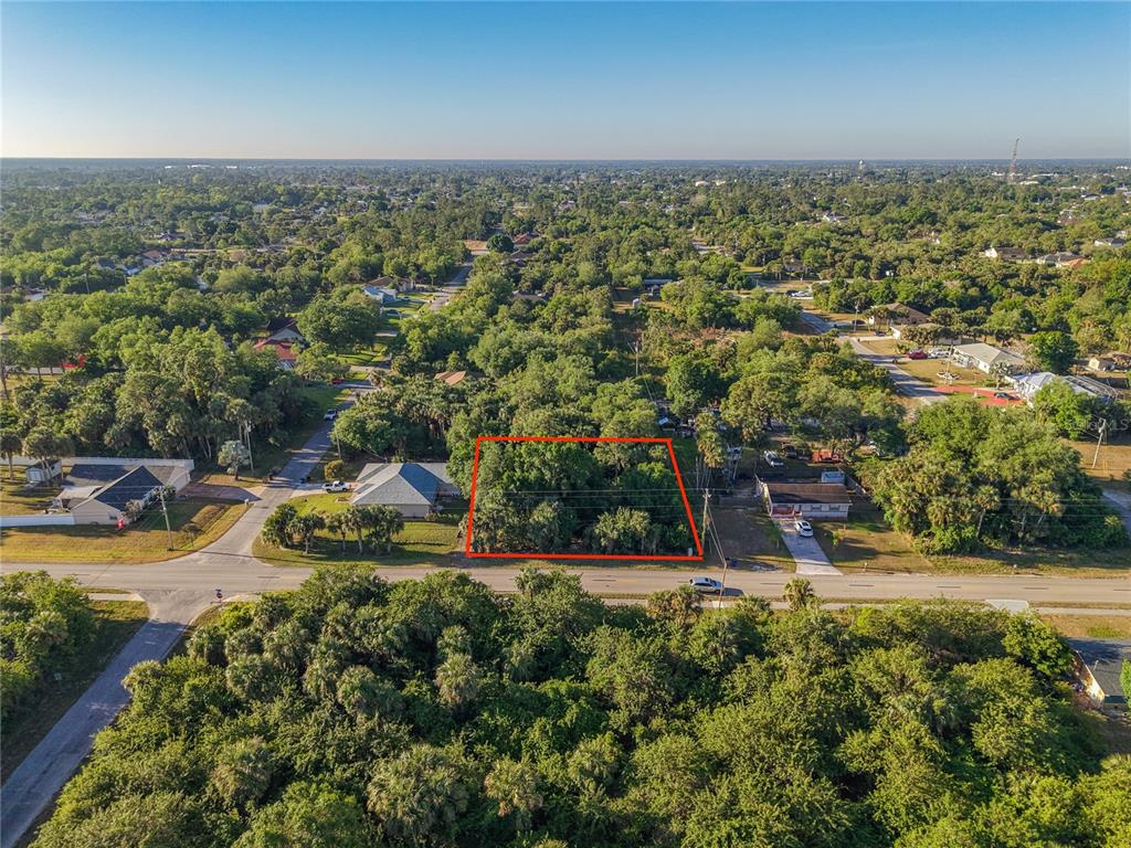 An aerial view shows a rectangular, tree-covered vacant lot outlined in red along a road — 103 W 6TH STREET, LEHIGH ACRES, FL