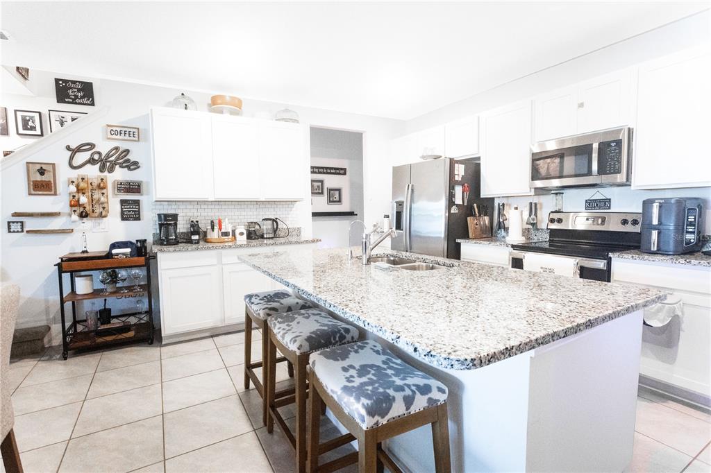 A kitchen features white cabinets, granite countertops, a central island with stools, and tile flooring — 643 BELGROVE STREET, DEBARY, FL