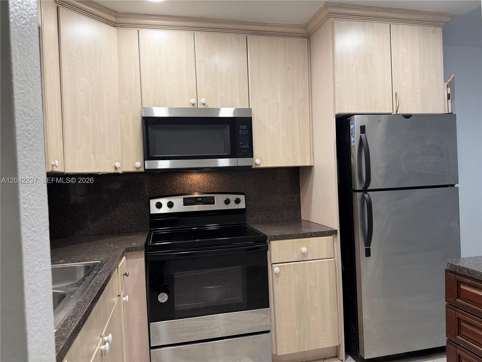 A kitchen features light wood cabinets, stainless steel appliances, and dark speckled countertops — NORTH MIAMI BEACH, FL