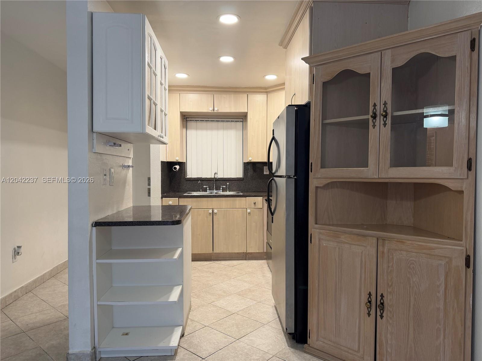 A kitchen features light wood cabinets, a black countertop, and a white freestanding shelving unit — NORTH MIAMI BEACH, FL